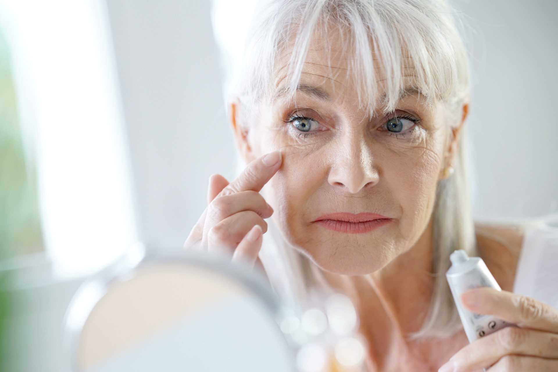 Portrait of senior woman applying anti-aging cream. 
